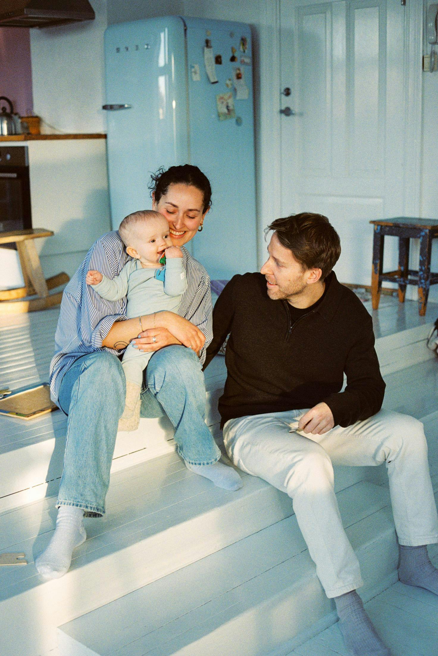 A family of three are sitting on a white wood floor