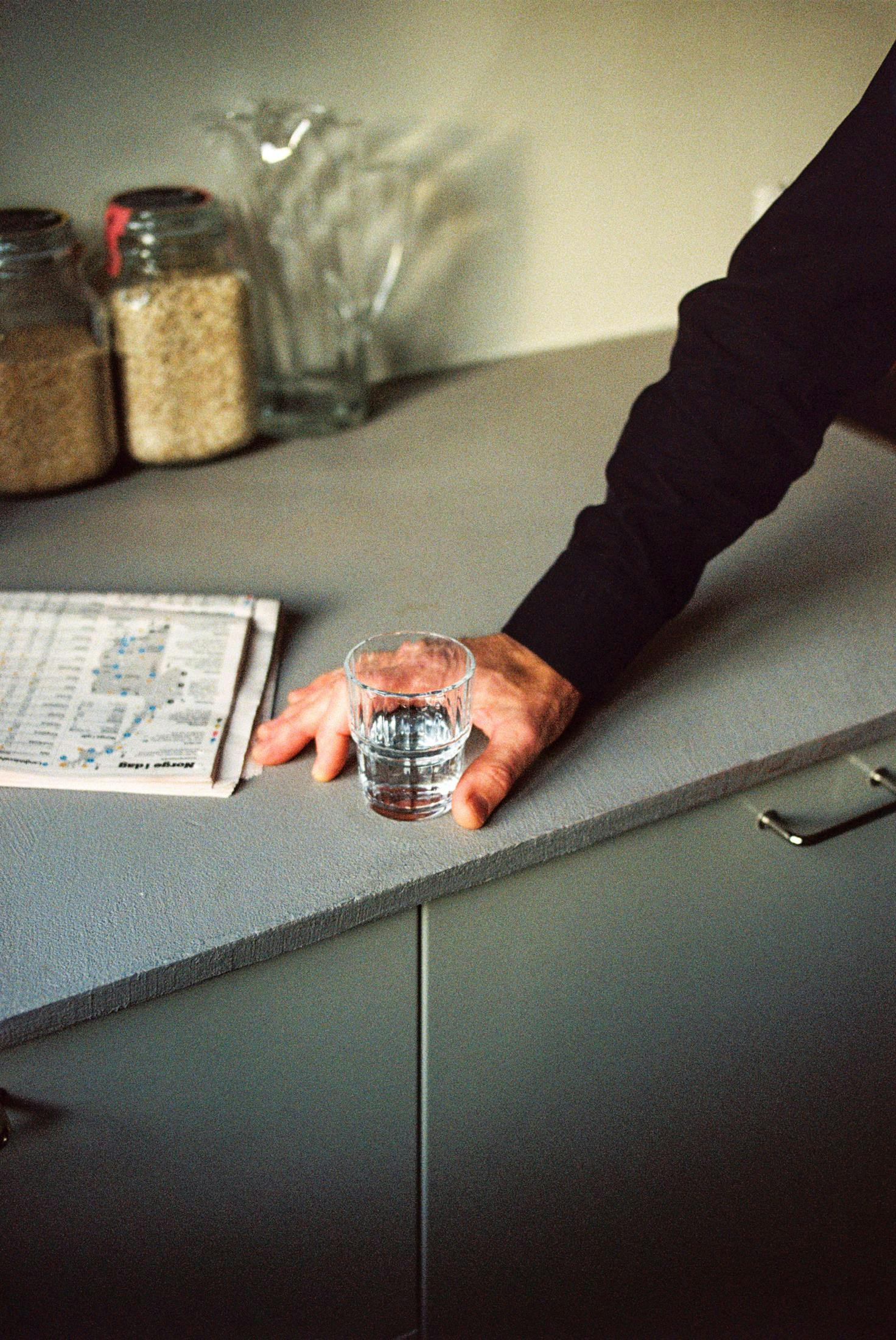 An image of a man holding a glass of water on a kitchen countertop